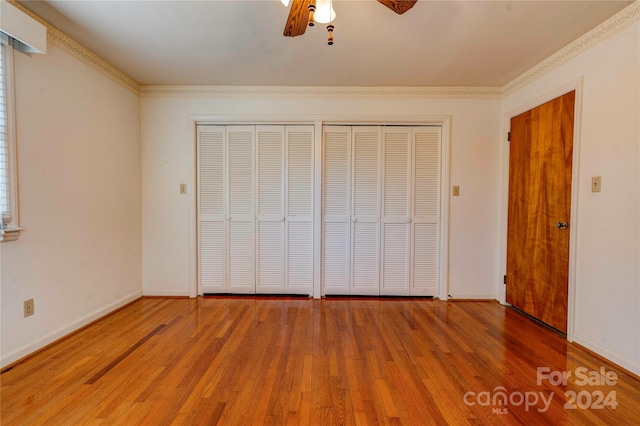 unfurnished bedroom featuring ceiling fan, hardwood / wood-style flooring, and multiple closets