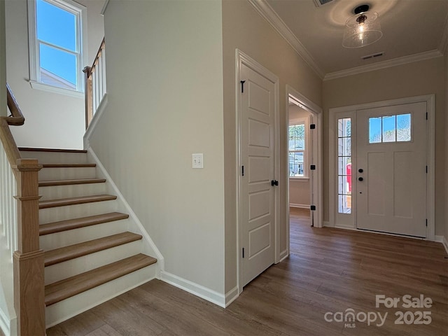 foyer entrance featuring wood finished floors, visible vents, stairs, ornamental molding, and plenty of natural light