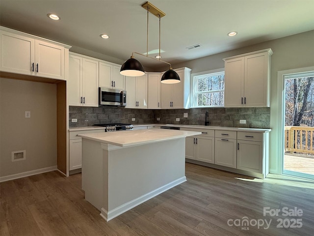 kitchen with stainless steel microwave, range, visible vents, and white cabinets