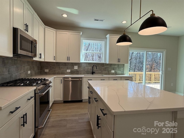 kitchen featuring visible vents, a kitchen island, a sink, stainless steel appliances, and backsplash