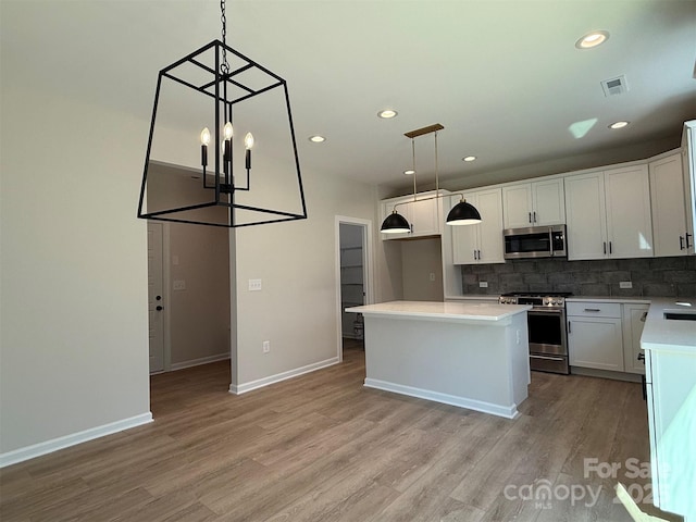 kitchen featuring stainless steel appliances, a kitchen island, visible vents, light wood-type flooring, and backsplash