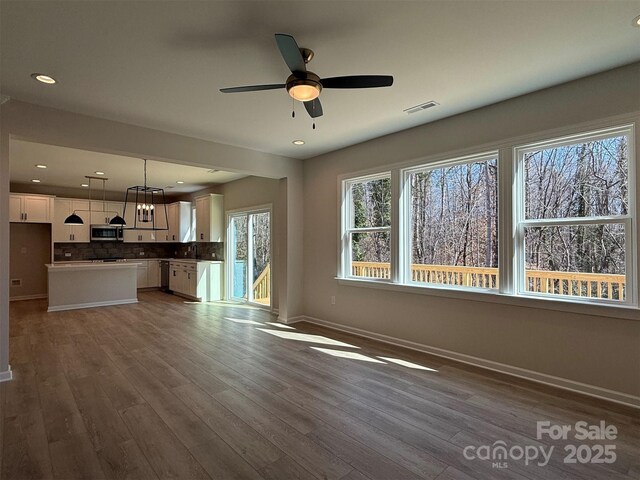 unfurnished living room featuring a sink, visible vents, baseboards, and wood finished floors