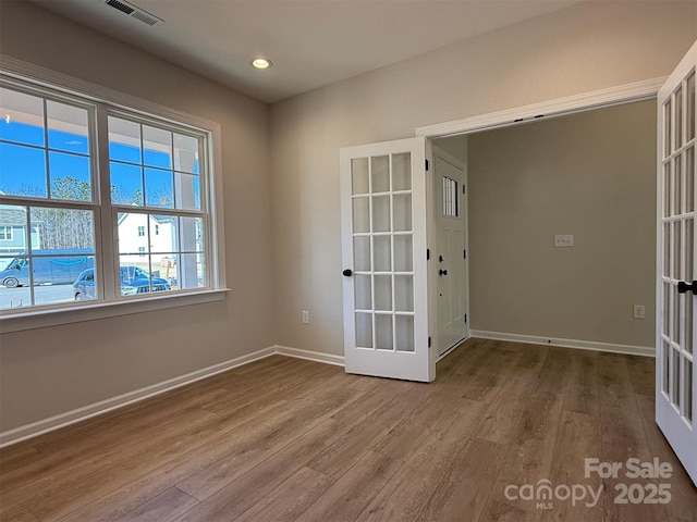 spare room featuring french doors, visible vents, baseboards, and wood finished floors