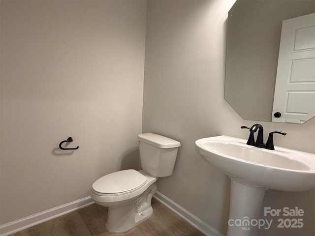 half bath with wood finished floors, toilet, and baseboards