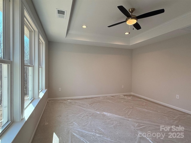 empty room with ornamental molding, a tray ceiling, visible vents, and baseboards