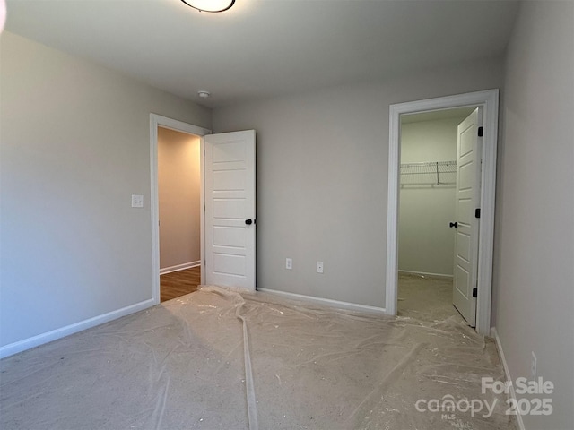 unfurnished bedroom with a spacious closet, a closet, and baseboards