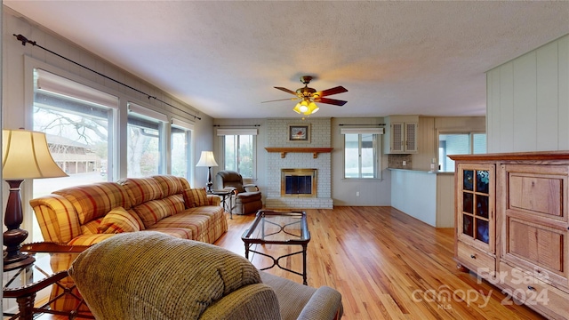 living room featuring wood walls, ceiling fan, a textured ceiling, a fireplace, and light wood-type flooring