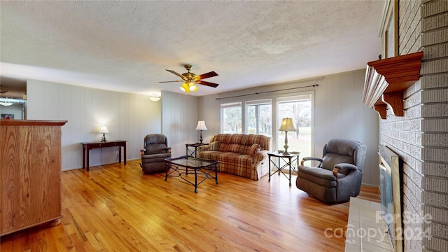 living room with a fireplace, a textured ceiling, ceiling fan, and light hardwood / wood-style flooring