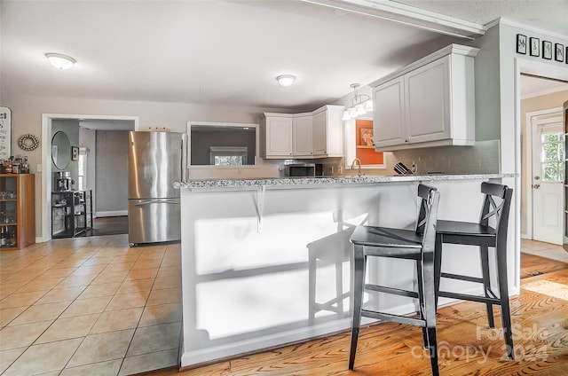 kitchen with white cabinetry, kitchen peninsula, a kitchen bar, and stainless steel fridge