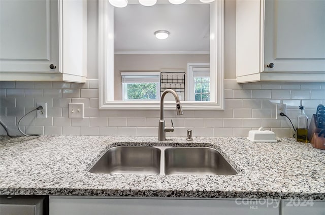 kitchen featuring backsplash, sink, light stone countertops, and white cabinets