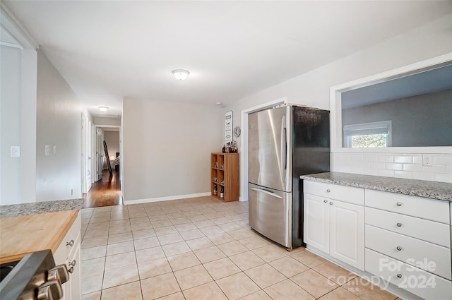 kitchen featuring white cabinets, butcher block countertops, light tile patterned flooring, backsplash, and stainless steel fridge