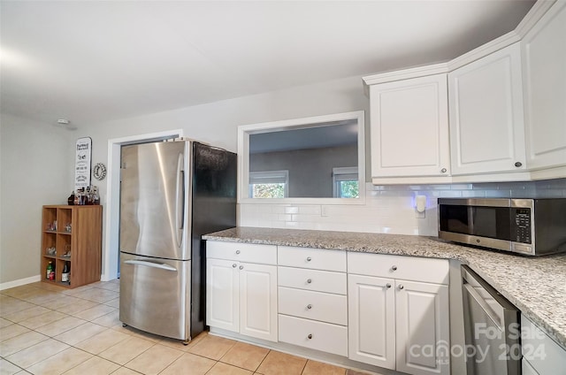 kitchen with stainless steel appliances, light tile patterned flooring, light stone countertops, backsplash, and white cabinets