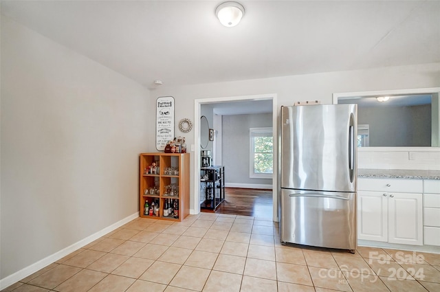 kitchen with white cabinetry, light stone countertops, light tile patterned floors, lofted ceiling, and stainless steel fridge