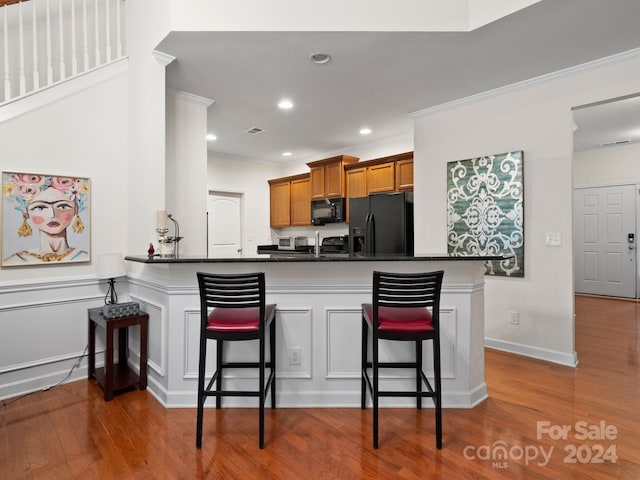 kitchen featuring a breakfast bar area, kitchen peninsula, black appliances, and wood-type flooring