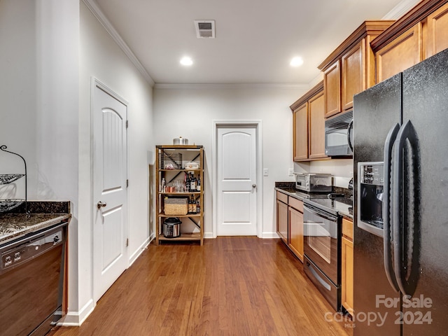 kitchen featuring dark stone countertops, crown molding, black appliances, and hardwood / wood-style flooring