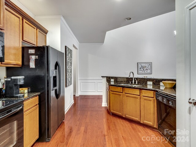 kitchen featuring ornamental molding, black appliances, sink, dark stone countertops, and light hardwood / wood-style floors