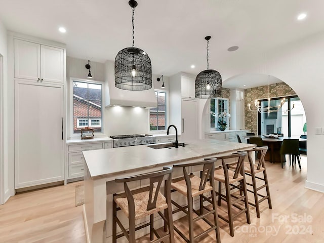 kitchen with a center island with sink, white cabinetry, sink, and light hardwood / wood-style flooring