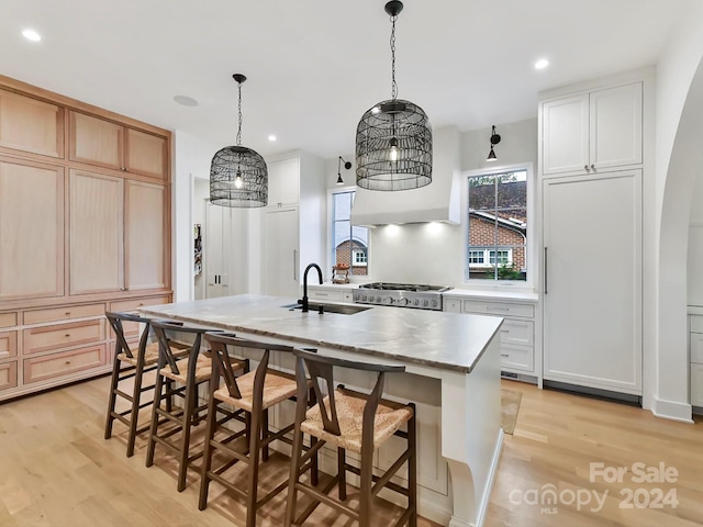 kitchen featuring light hardwood / wood-style floors, a center island with sink, hanging light fixtures, sink, and stainless steel range