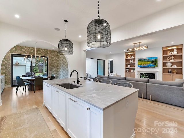 kitchen with a center island with sink, sink, light stone counters, white cabinets, and pendant lighting