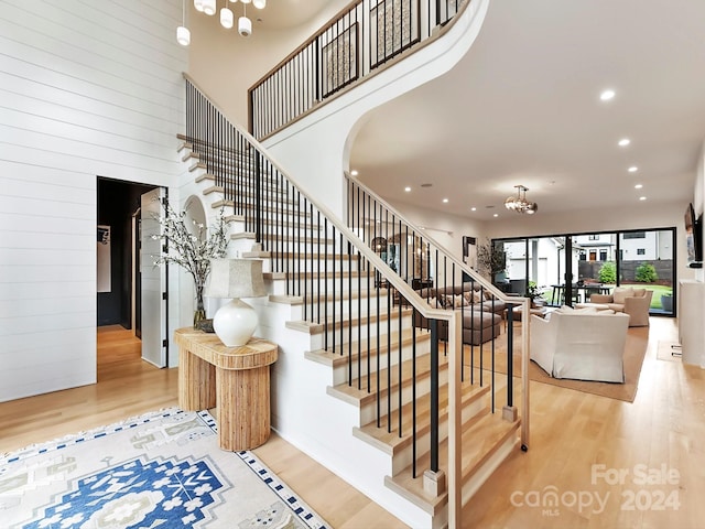 stairs with hardwood / wood-style floors, wooden walls, an inviting chandelier, and a towering ceiling