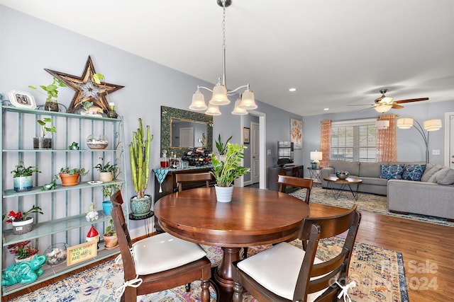 dining space with ceiling fan with notable chandelier and hardwood / wood-style flooring