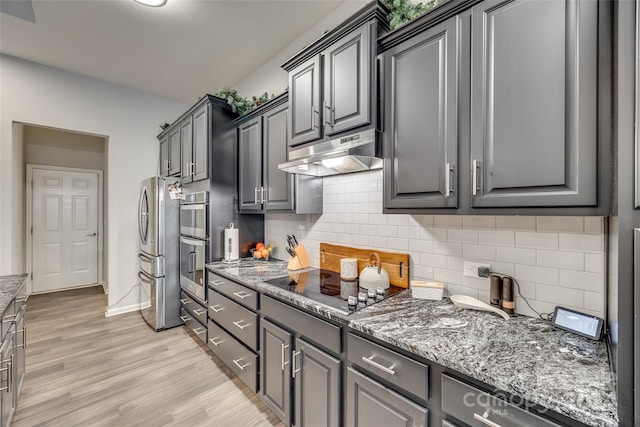 kitchen featuring appliances with stainless steel finishes, tasteful backsplash, dark stone counters, light hardwood / wood-style flooring, and gray cabinets