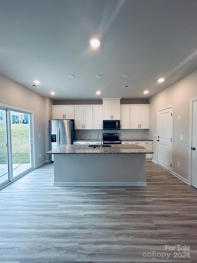 kitchen with white cabinets, light hardwood / wood-style floors, stainless steel appliances, and an island with sink