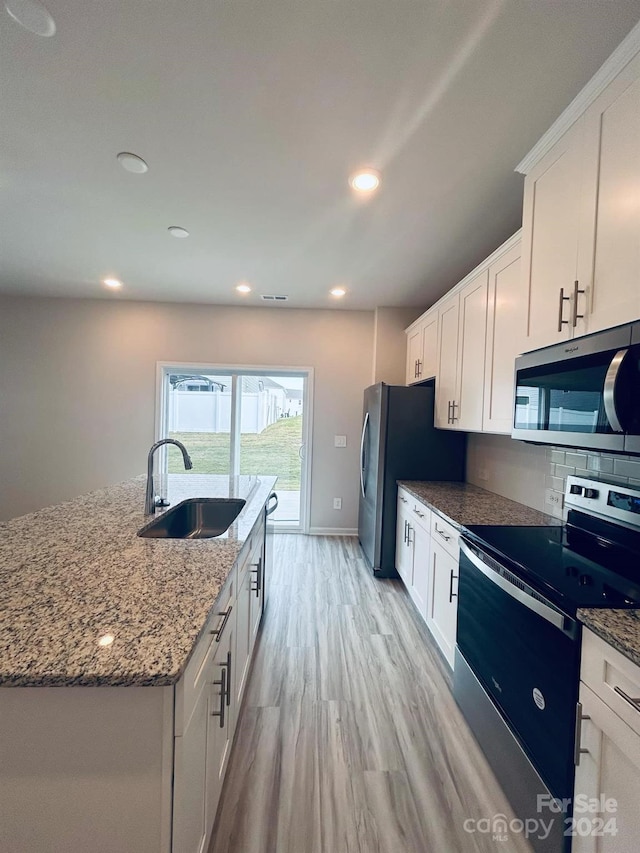 kitchen featuring sink, light hardwood / wood-style flooring, an island with sink, white cabinetry, and stainless steel appliances