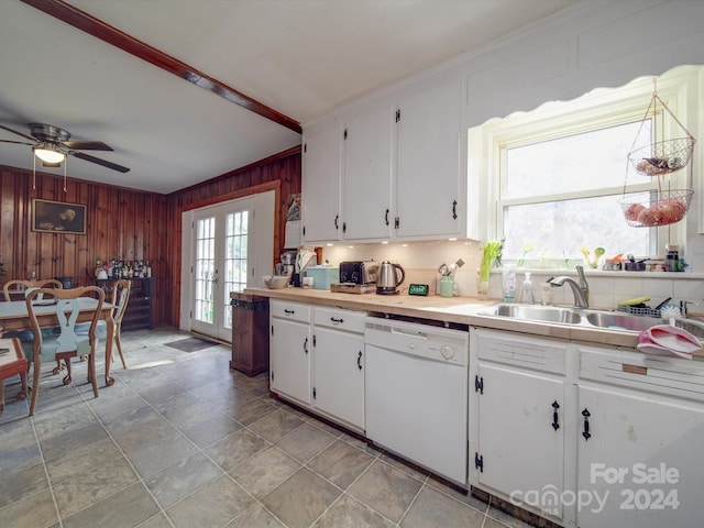 kitchen with french doors, white dishwasher, wooden walls, sink, and white cabinets