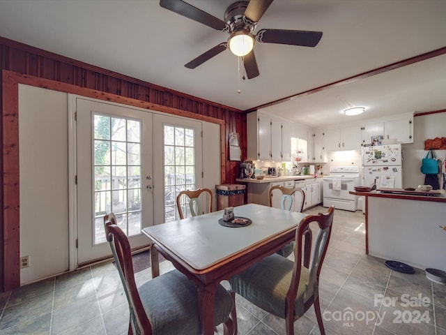 tiled dining space with french doors, ornamental molding, ceiling fan, and wooden walls