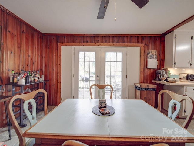 dining space featuring french doors, crown molding, ceiling fan, and wooden walls