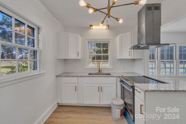 kitchen featuring island exhaust hood, stainless steel range with electric cooktop, white cabinetry, decorative backsplash, and sink