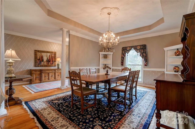 dining area with a chandelier, decorative columns, ornamental molding, a raised ceiling, and light wood-type flooring