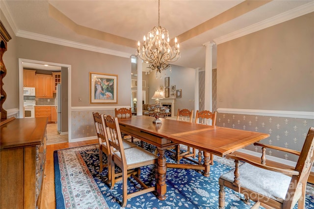 dining area with decorative columns, a chandelier, ornamental molding, and light hardwood / wood-style flooring