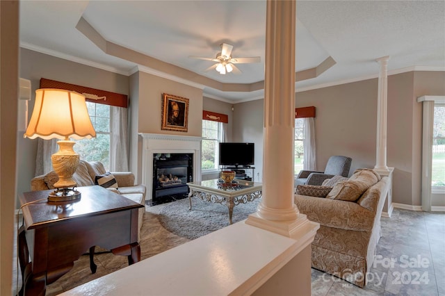 living room featuring ornamental molding, ceiling fan, a tray ceiling, and ornate columns