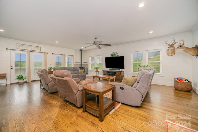 living room with plenty of natural light, ceiling fan, a wood stove, and light hardwood / wood-style flooring