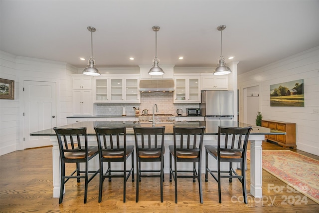 kitchen featuring white cabinets, pendant lighting, a center island with sink, and light hardwood / wood-style floors