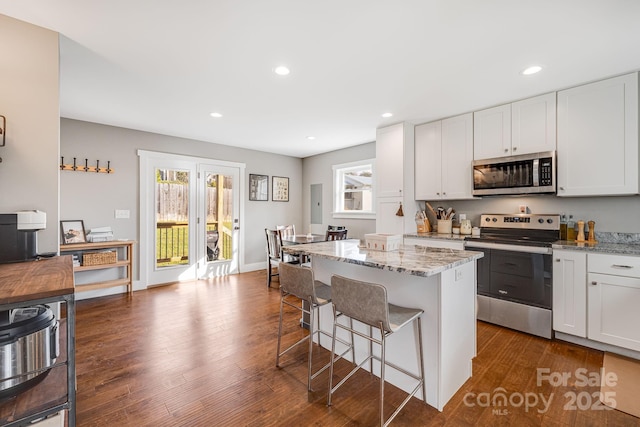 kitchen with stainless steel appliances, white cabinetry, a center island, and light stone counters