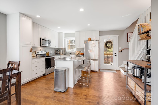 kitchen with a breakfast bar area, stainless steel appliances, light stone countertops, white cabinets, and a kitchen island