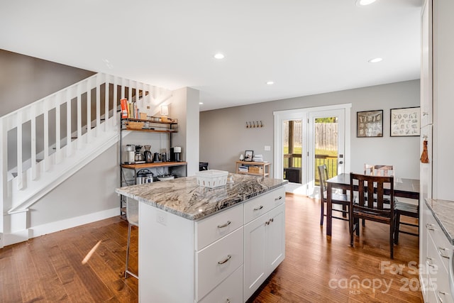 kitchen featuring white cabinetry, hardwood / wood-style floors, light stone counters, and a kitchen island