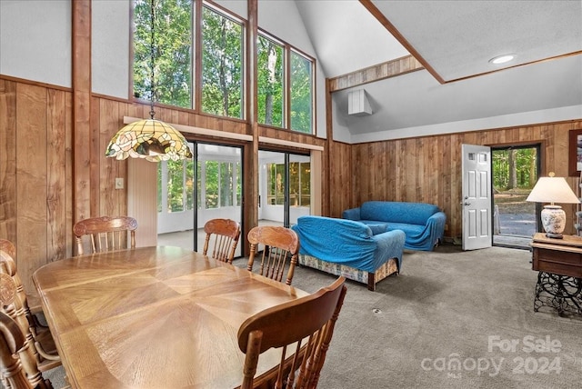 carpeted dining space with high vaulted ceiling, a wealth of natural light, and wooden walls