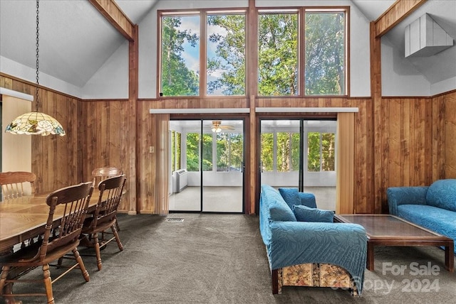 interior space featuring carpet flooring, high vaulted ceiling, wood walls, and ceiling fan