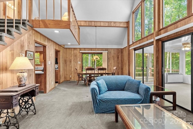 carpeted living room featuring ceiling fan, wooden walls, and high vaulted ceiling