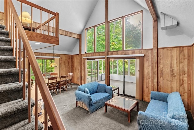 carpeted living room with high vaulted ceiling, beamed ceiling, wooden walls, and a healthy amount of sunlight