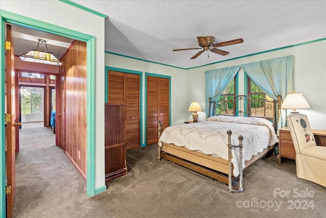 bedroom with ceiling fan, a textured ceiling, carpet flooring, and two closets