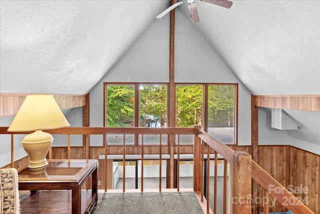 interior space with high vaulted ceiling, wooden walls, a textured ceiling, and ceiling fan