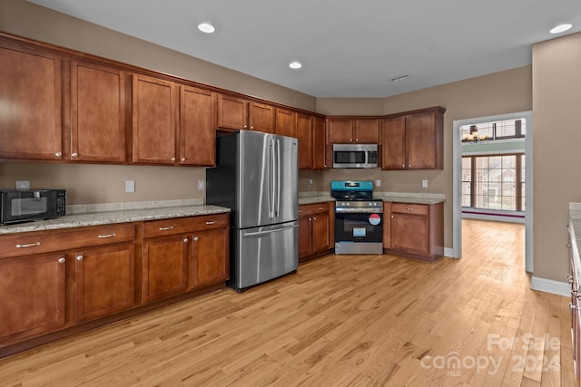 kitchen with light stone counters, light wood-type flooring, appliances with stainless steel finishes, and an inviting chandelier