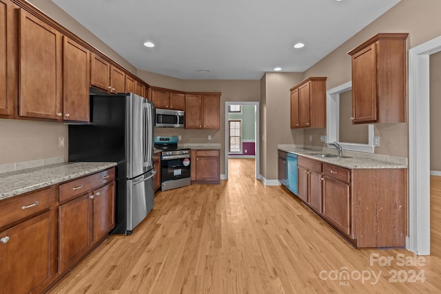 kitchen with light stone countertops, light hardwood / wood-style flooring, stainless steel appliances, and sink