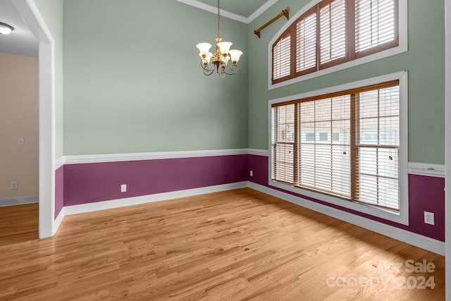 spare room with ornamental molding, light hardwood / wood-style flooring, a towering ceiling, and an inviting chandelier