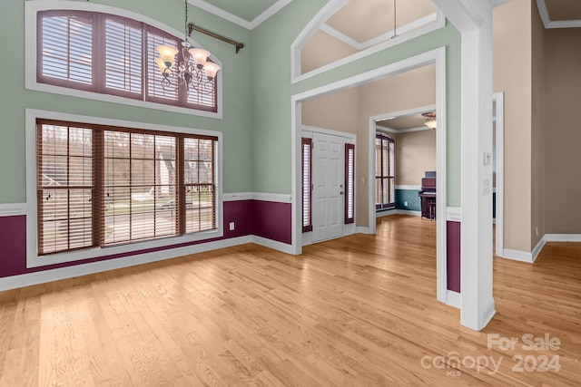 foyer entrance featuring hardwood / wood-style floors, ornamental molding, a towering ceiling, and a chandelier